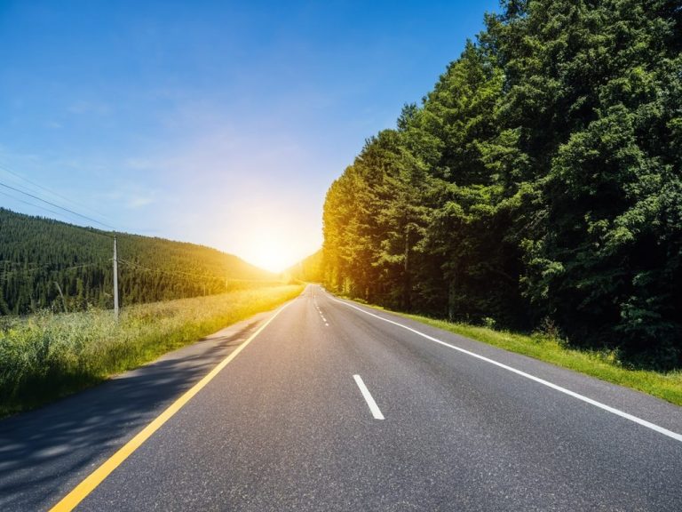 Sonnenaufgang über einer Landstraße, umgeben von Bäumen und Wiesen.